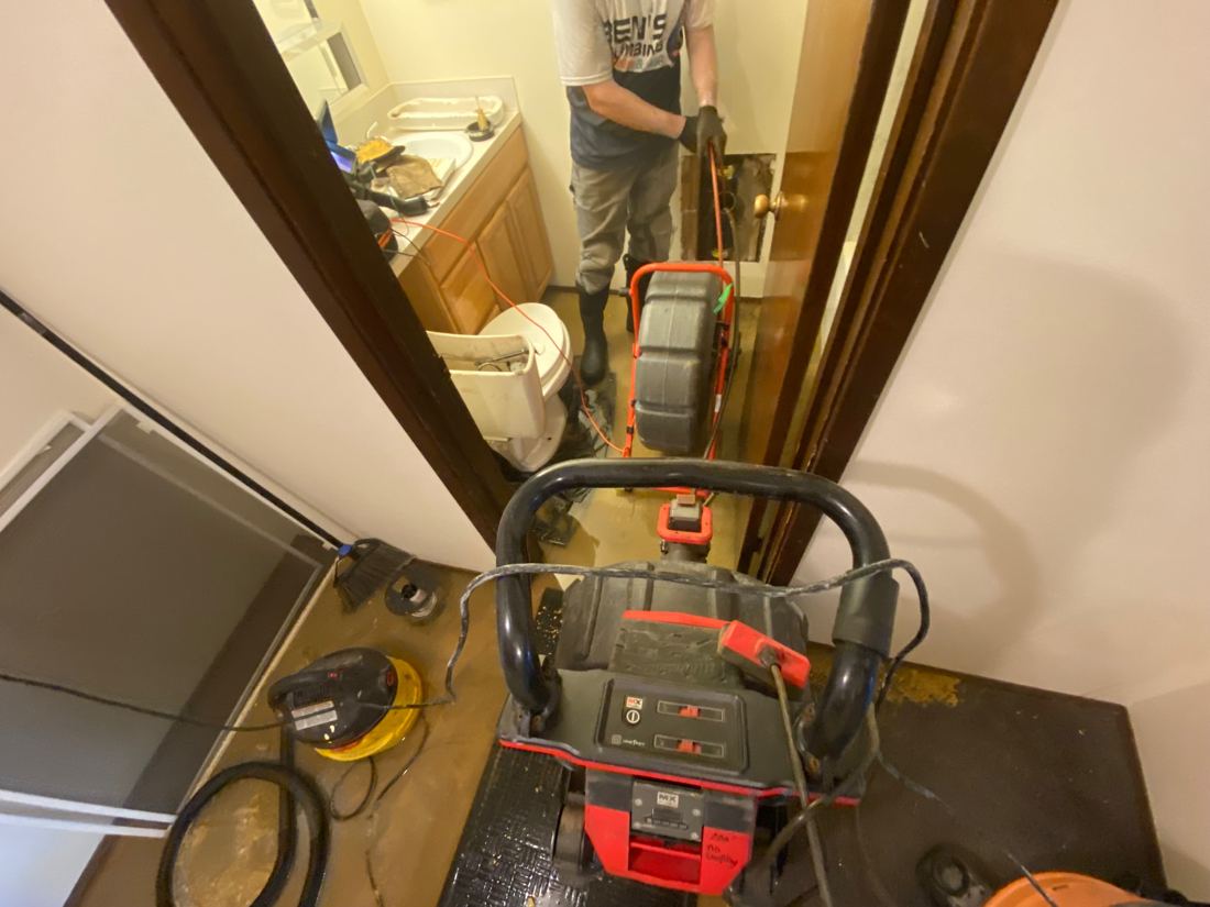 Soundview technician running a drain machine beside a bathroom vanity during sewage cleanup